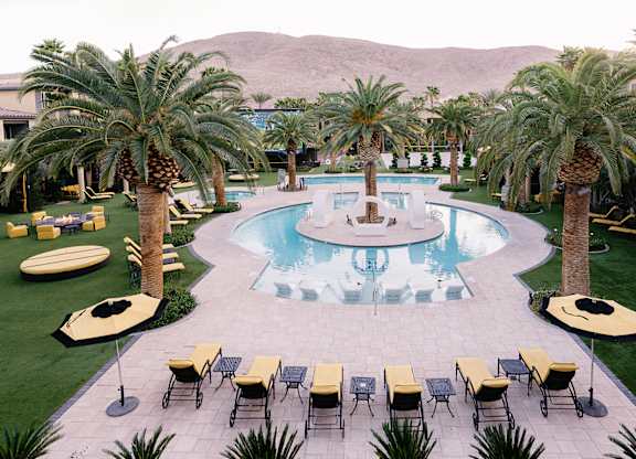 A pool surrounded by palm trees and lounge chairs.