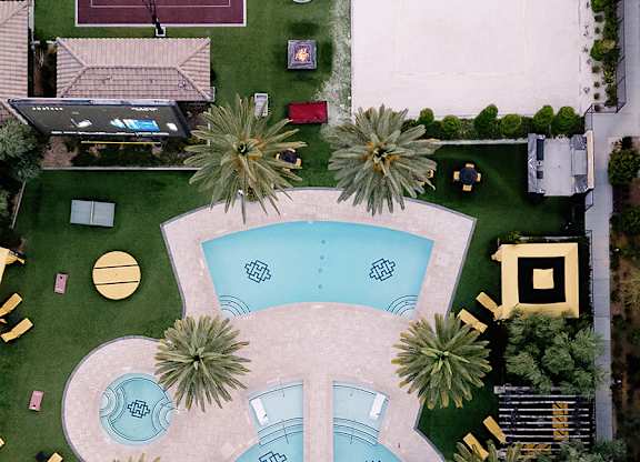 A tennis court is surrounded by a pool and palm trees.