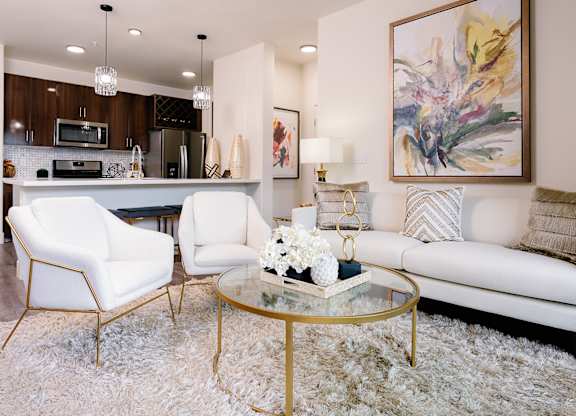 A modern living room with a white sofa, two white chairs, and a glass coffee table.
