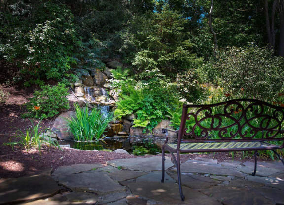 a bench sits on a stone patio next to a pond at Monroeville Apartments, Monroeville, PA