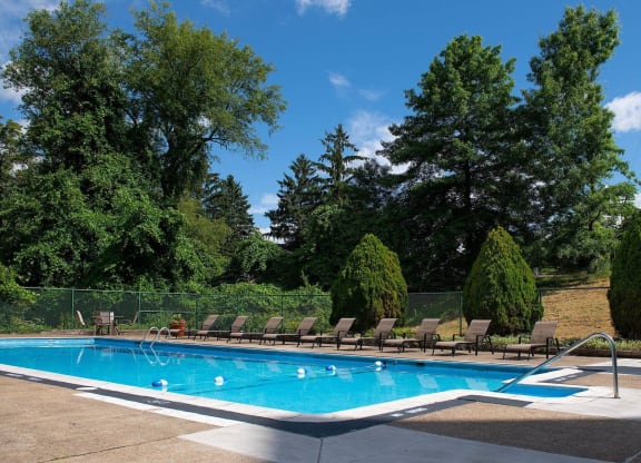 a swimming pool with chaise lounge chairs and trees in the background at Monroeville Apartments, Monroeville, 15146