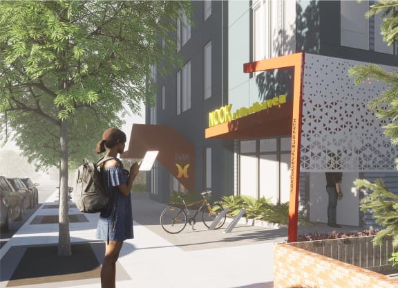 A rendering of a person is walking on a sidewalk with a backpack and a book in hand in front of an apartment building at Nook at Northaven Apartments, Seattle, 98125