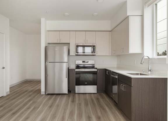 A modern kitchen with a refrigerator, microwave, oven, and sink at Nook at Northaven Apartments, Seattle, 98125