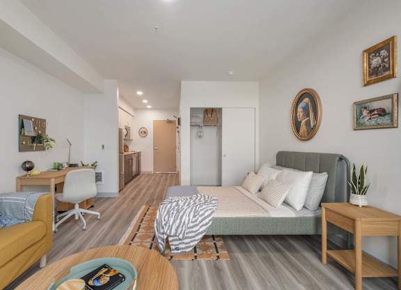 A living room with a yellow couch, a grey bed, and a wooden table at Nook at Northaven Apartments, Seattle, Washington