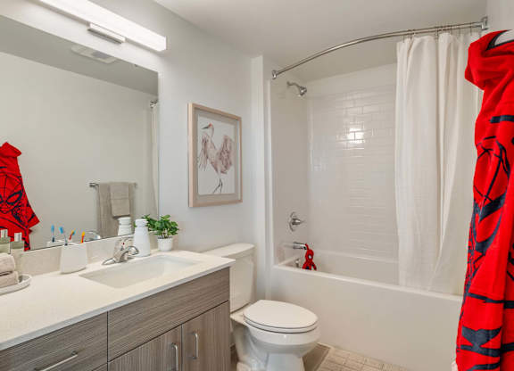A bathroom with a white toilet, a white sink, and a red robe at Nook at Northaven Apartments, Seattle, WA 98125