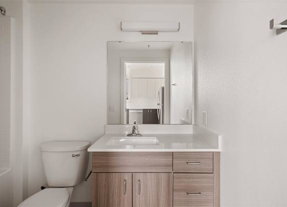 A white bathroom with a toilet, sink, and mirror at Nook at Northaven Apartments, Washington