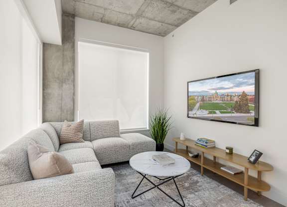 A living room with a grey couch, a white coffee table, and a flatscreen television on the wall.