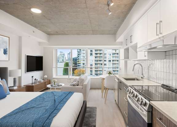 A modern living space with a large bed, a sofa, a flatscreen television, and a kitchen area.