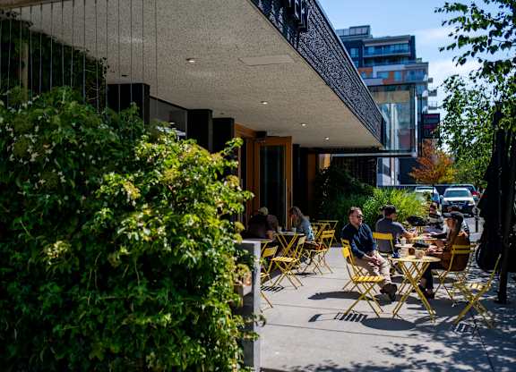 A group of people are sitting at tables outside of a coffee shop.