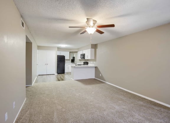 a living room with a ceiling fan and a kitchen in the background