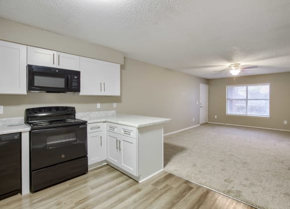 a kitchen and living room with white cabinets and a black stove top oven