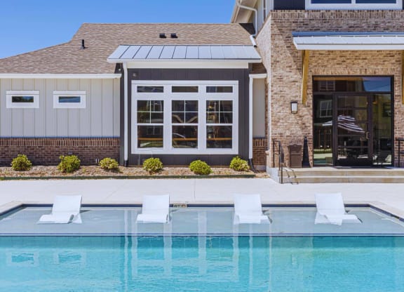 a swimming pool in front of a house with a pool and chairs