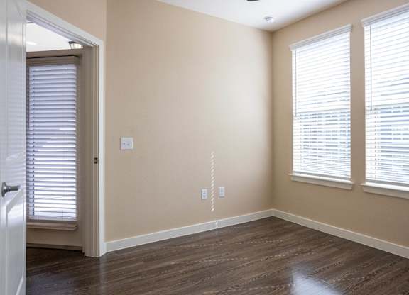 A room with wooden floors and two windows with blinds.