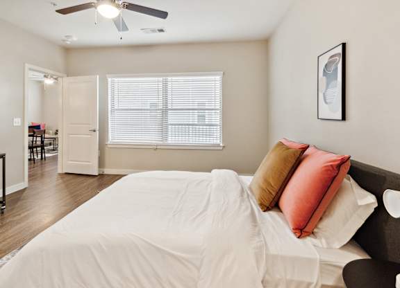 A bedroom with a bed, a ceiling fan, and a window with blinds.