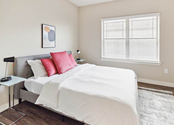 A bedroom with a large bed and a window with blinds.