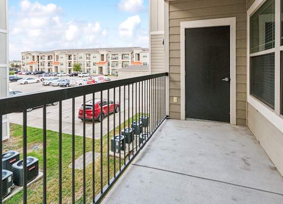 A balcony with a black railing and a red car parked in the parking lot.