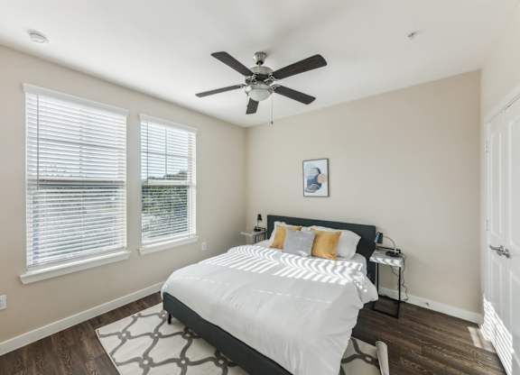 A bedroom with a bed, a ceiling fan, and a window with blinds.