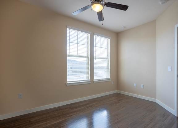 an empty living room with a ceiling fan and two windows