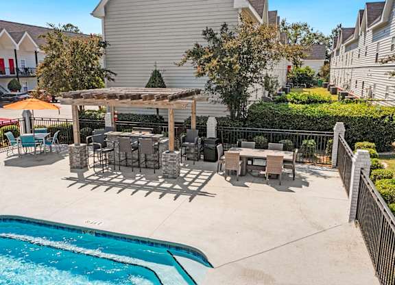A pool with a table and chairs and a grill in the backyard.