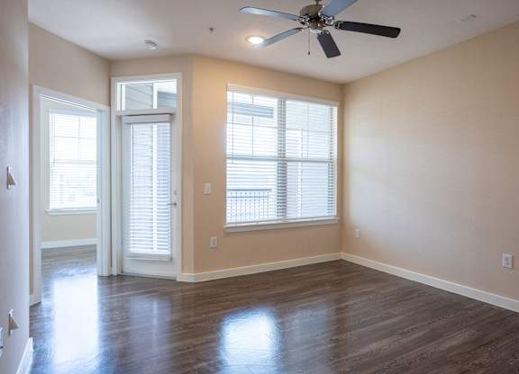 an empty living room with a ceiling fan and windows