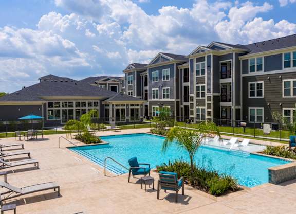 A large swimming pool surrounded by lounge chairs and a building in the background.