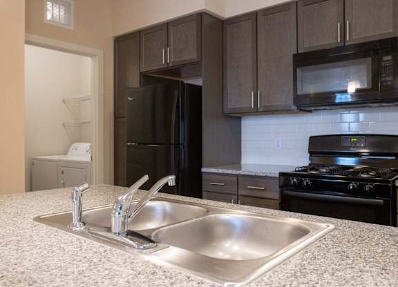 A kitchen with a sink, refrigerator, microwave, and stove.