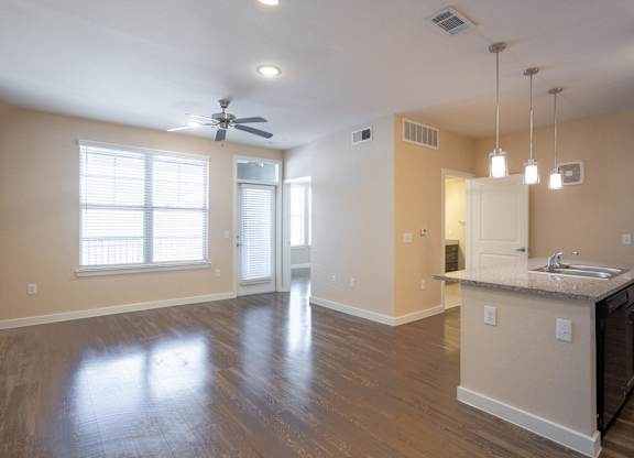 an empty living room with a kitchen and a ceiling fan