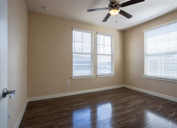 A room with a ceiling fan and two windows.