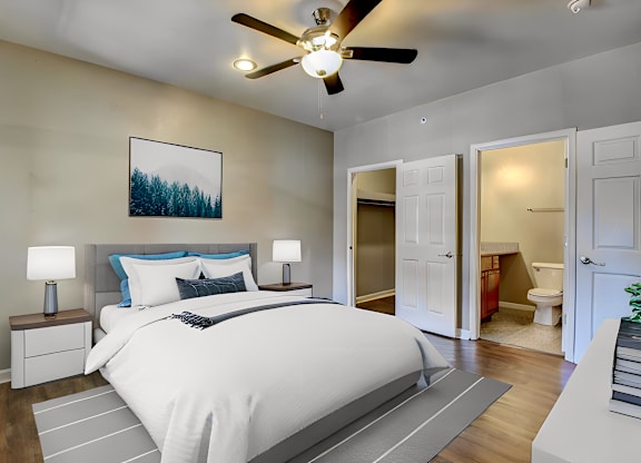 A bedroom with a large bed, a ceiling fan, and a painting of a forest on the wall.
