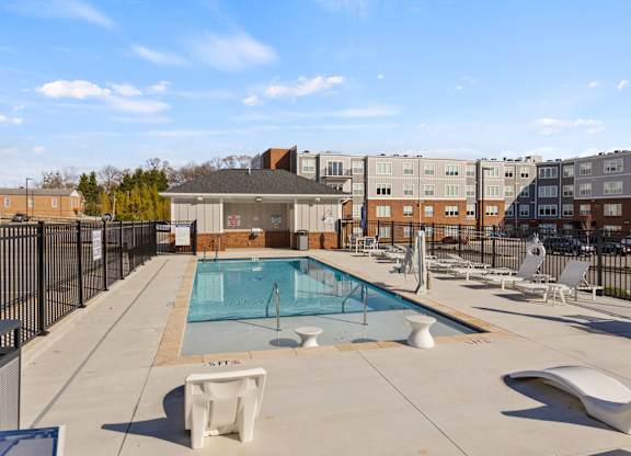 A pool surrounded by chairs and a fence.