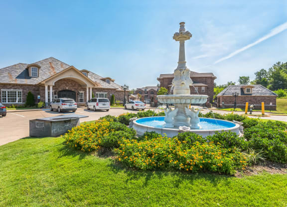 a fountain in front of a house with cars parked in a parking lot