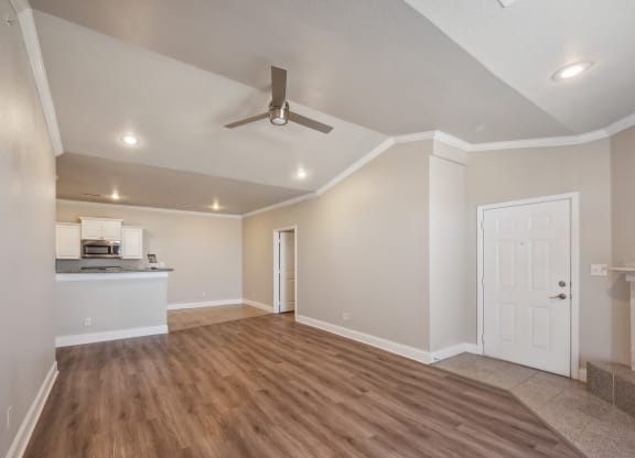 an empty living room with a ceiling fan and a kitchen