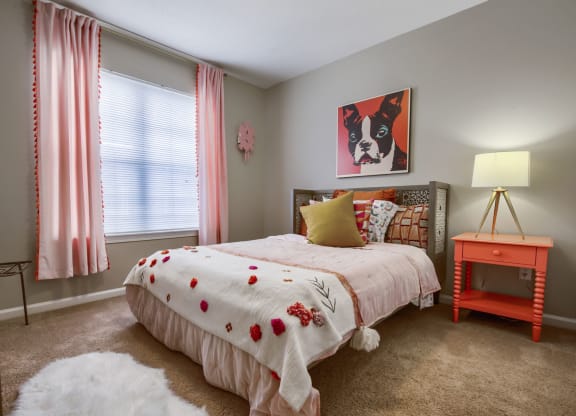a bedroom with a bed and a nightstand with a lamp and a painting of a dog