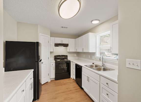 A kitchen with white cabinets and a black fridge.