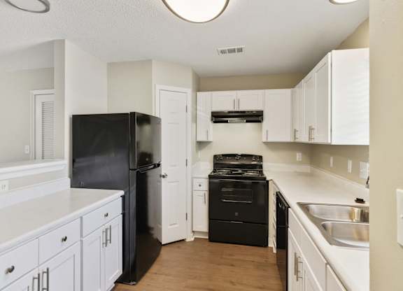 A black refrigerator is in a kitchen with white cabinets.