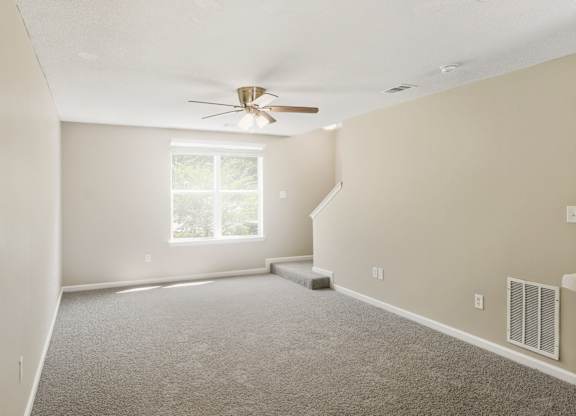 A room with a ceiling fan and carpeted floor.