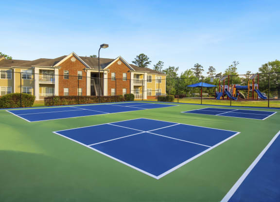a blue and green tennis court with yellow apartments in the background