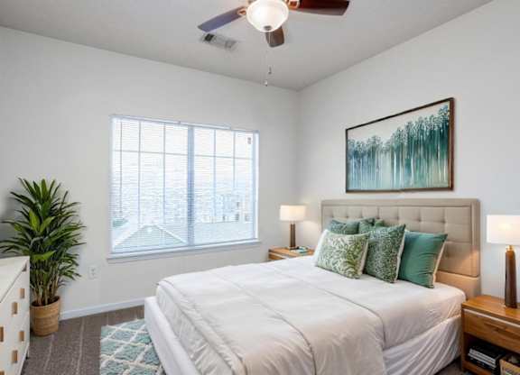 A bedroom with a large bed, a ceiling fan, and a painting on the wall.