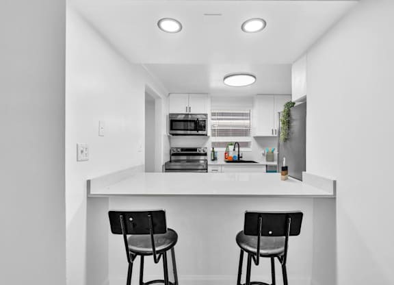 A kitchen with white cabinets and a white countertop with two black chairs.