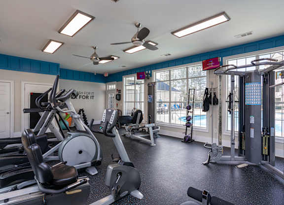 a gym with cardio equipment and windows with a view of a pool