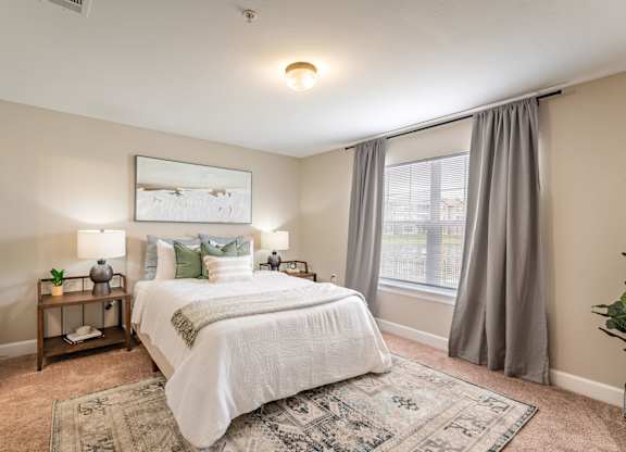 A bedroom with a large bed and a window with curtains.