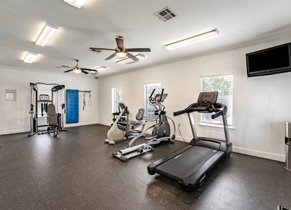 A spacious home gym with a treadmill, elliptical machines, and a fan.