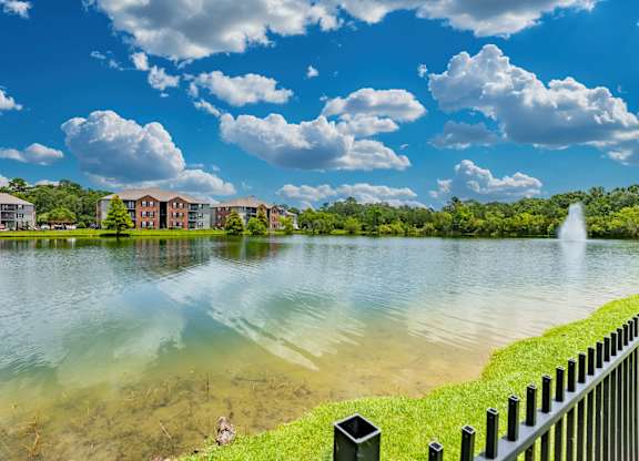 A serene lake with a fountain in the distance and apartment buildings in the background.