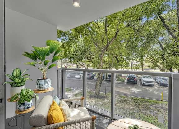 A balcony with a couch, plants, and a view of a parking lot.