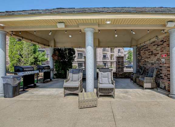 A covered patio area with chairs and a grill.
