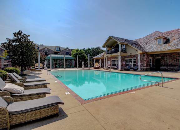A large outdoor swimming pool surrounded by lounge chairs and a building in the background.