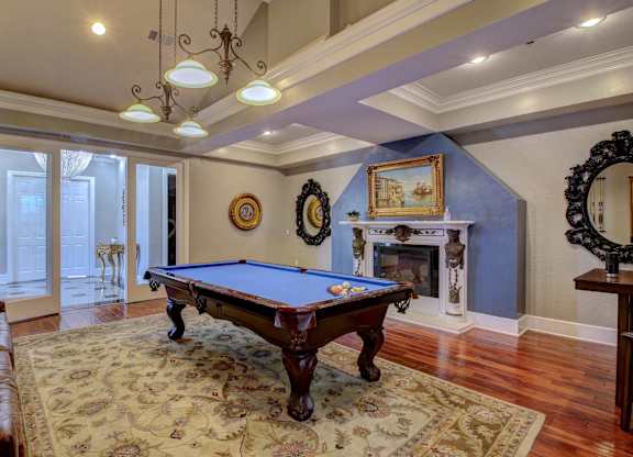 A pool table is in the middle of a room with a fireplace and a mirror.