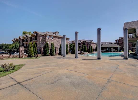 A concrete patio with four pillars in the middle and houses in the background.