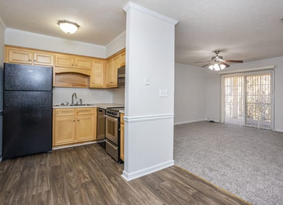 an empty living room with a kitchen and a ceiling fan