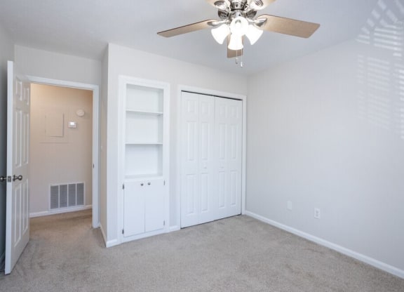 an empty bedroom with a ceiling fan and closet